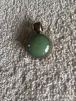 Front view of round green stone pendant set in polished silver on textured white background.