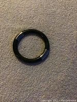 Top view of circular jade bangle bracelet with silver clasps on textured light gray surface