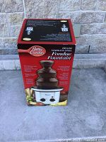 Photo of the unopened Betty Crocker Deluxe Stainless Steel Chocolate Fondue Fountain box showing front with product image and features.