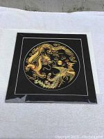 Silk embroidery art with two dragons in gold and colorful threads on black fabric, shown flat with plastic protective cover.