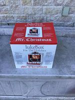 Photo of the closed original box of Mr. Christmas Jukebox For The Holidays showing front and side with product features and branding.
