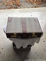 Top view of the closed briefcase showing patterned fabric with brown leather trim and brass combination lock hardware.