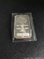 Front view of the silver bar in sealed plastic case on a black surface, showing the profile portrait and purity markings.