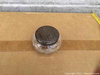 Photo showing crystal dish with visible round sterling silver lid resting on top, placed on cardboard background.
