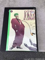 Front cover of The Greatest Joker Stories Ever Told hardcover book featuring the Joker with a trick gun, still sealed in plastic cover with original price tag.