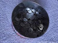 Overhead photo showing the interior of a Coca-Cola metal tin filled with American coins including quarters, nickels, and dimes, with surface reflections visible.