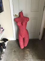 Front view of the pink wicker female manikin bust standing against a door, highlighting its height and overall form.