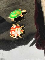 Green turtle brooch with hand-painted shell and the red ladybug brooch with rhinestone accents on black surface.