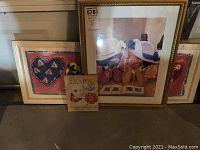 Three pieces of art shown: small canvas in front, large framed print center, medium framed print in background