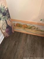 Photo shows a framed landscape painting with autumnal trees, measure about 40x15 inches, leaning against wall and floor.