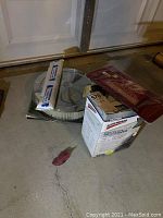 Items arranged on garage floor, including air cleaner assembly, Kraco seat cover in plastic, lift supports in box.