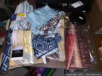 Fabric shower curtains and bath mats assorted on a table with various patterns in blues, yellows, grays, and browns.