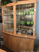Full view of the blonde china cabinet showing glass doors with shelves inside and lower storage with wooden doors.