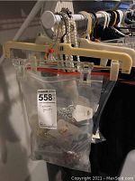 Two clear plastic bags hanging with various loose necklaces including faux pearls and chain types visible inside one bag