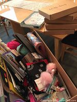 Photo showing an open box filled with assorted craft supplies including yarn, papers, bandannas, pens, and other materials.