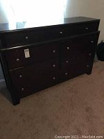 Front view of large dark brown wooden dresser showing nine drawers with metal knob handles.