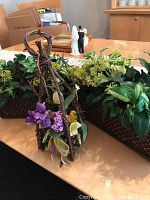 Front view of three faux flower arrangements in woven baskets on dining table with decorative floral grapevine holder hanging in front