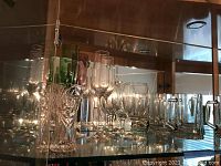 Shelf with assorted glassware including clear wine glasses, pilsner glasses, mugs, and some decorative crystal-style glasses.