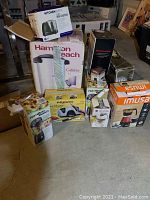 Lot with all kitchen appliances boxed and arranged together, showing coffee maker, blenders, griddle, mini chopper, and sharpener.