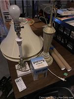 Two table lamps, one white-based with bulb and the other beige fluted with metal detailing, two large cream lampshades, Himalayan salt lamp box, UV bulbs and cords shown.