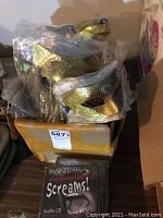 Box filled with multiple plastic-wrapped gold and blue masquerade masks plus an audio CD titled 'Screams!' in front