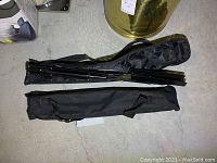 Two folded music stands inside black fabric carrying cases placed on a concrete floor.