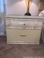 Front view of cream-colored nightstand showing two drawers and overall condition with water damage on top front area.