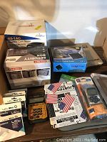 Photo showing several office items neatly arranged including calculator, ink cartridges boxes, coin sorter box, security box, and postal scale box