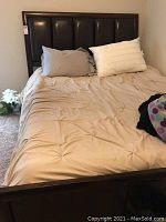 Full view of queen size bed with beige bedding and leather padded headboard framed in brown wood.