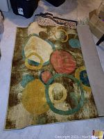 Full view of area rug showing geometric circular shapes in brown, gold, teal and cream colors.