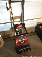 Full view of Toro Power Curve 1200 snow blower showing metal handlebar, red body with Toro label, and black plastic snow chute.