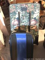 Two soft side suitcases stacked, floral large bag behind and Rockland Polo Equipment smaller bag in front.