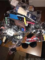 Pile of various sunglasses and reading glasses mostly in plastic packaging and original tags