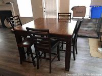 Full view of the dark wood square table with four ladderback chairs and two small bar stools around it