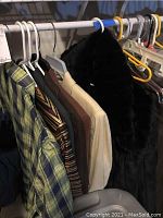 Photo showing women's clothing hanging on hangers including a green plaid shirt, multi-color striped knit top, a black faux fur jacket, and some neutral colored tops.