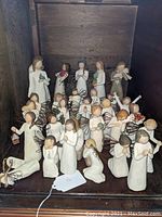 Photo showing collection of Willow Tree angel and human figurines on a wooden shelf with metal wire wings and carved wood features.