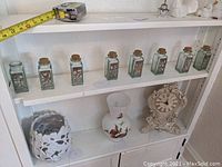 Shelf display of all 8 metal mounted glass spice jars, with seven cork stoppers present, one missing.