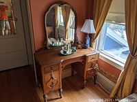 Full frontal view of wooden Art Deco lady's vanity with attached mirror and items on top.