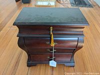 Closed bombe style wooden jewelry chest with dark brown finish and gold lock with tassel.