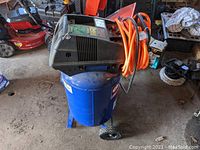 Full view of Campbell Hausfeld blue air compressor with black motor housing and attached orange hose, showing wheels and base.