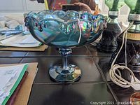 Blue iridescent carnival glass footed compote bowl shown from side view on a table.