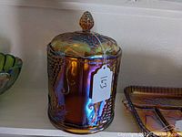 Front and side view of carnival glass cookie jar with lid, showing the grapevine embossed pattern and iridescent finish.