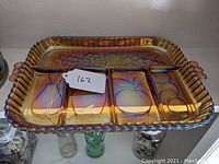 Top view of the iridescent carnival glass tray showing four divided sections with pear, apple, peach, and grape fruit motifs, scalloped edge and framed bead detail.