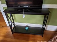 Front view of the black media table holding a TV, showing flat top and bottom shelf.