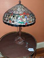 Full view of stained glass lamp on a brown table with floral and geometric motif and pull chains, bronze metal base.