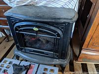 Front view of black electric faux wood stove with curved top and decorative front showing flame effect and logs behind glass panel.