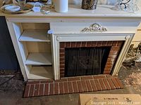 Full frontal view of white wooden mantel surround with faux brick interior, mesh screen and left-side bookshelf