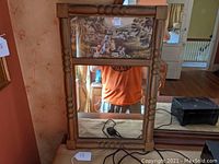 Full view of wood framed mirror with top section containing a country scene print depicting a rural landscape with children and sheep.