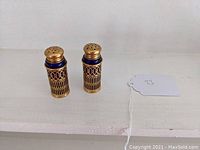 Pair of cobalt glass salt and pepper shakers with gilt metal cage mounts shown on a white surface with a price tag nearby.