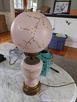 Full view of the pink glass table lamp with cherry blossom floral design on globe shade and vase-shaped base.